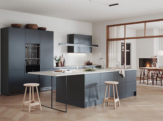 Mørkegrå kjøkkenøy med lys benkeplate, lyse treskamler, lyst tregulv og åpen spisestue med peis.