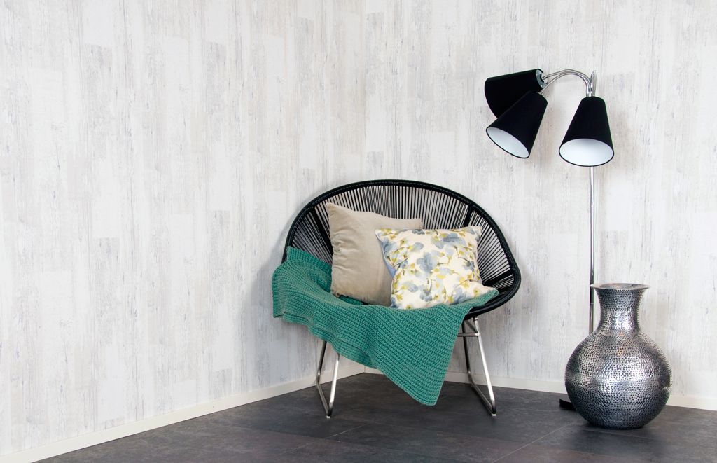 Svart trådstol mot hvit panelvegg, med grønt pledd og blomstrete pute, ved sølv vase og gulvlampe