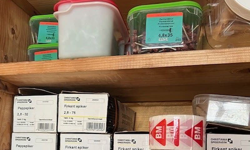 Tre-hylle med plastbeholdere med grønne og røde lokk, og merkede bokser med spiker.