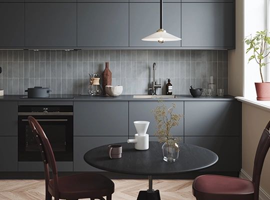 Moderne grått kjøkken med mørke skap, rundt bord med to stoler og en hengelampe over spisebordet.
