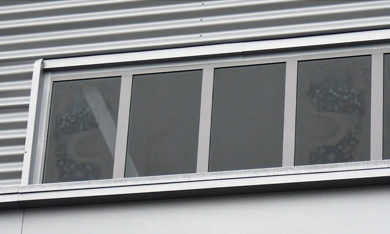 Smalt rektangulært vindu med fire mørke glassfelt i sølvgrå korrugert metallvegg.