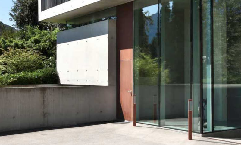 Moderne betongbygg med glassfasade, rødt ståldør og grønt landskap i bakgrunnen.