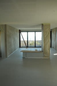 Uferdig rom med grått betonggulv, hvite vegger, plastbeskyttede søyler og stort vindu mot ute.