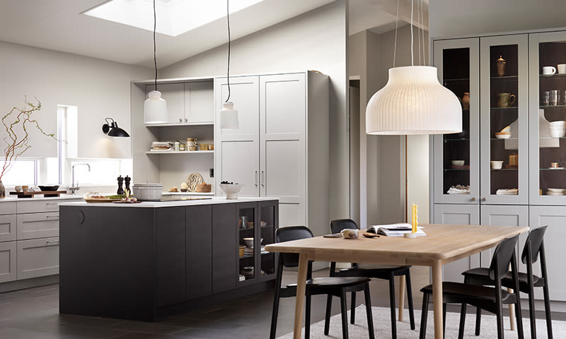 Moderne kjøkken med lysgrå skap, mørk øy, trebord med svarte stoler og hengelamper.
