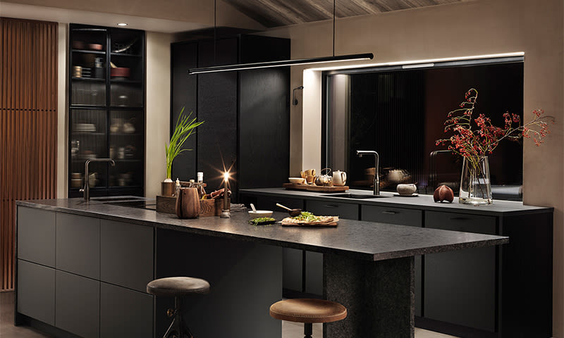 Moderne mørkt kjøkken med stor svart kjøkkenøy, varme treinnslag, stearinlys og røde bærkvister.