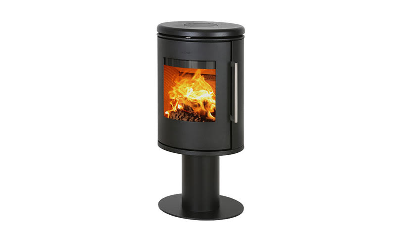 Sort sylinderformet vedovn med glassdør på sokkel, glødende oransje flammer innvendig.