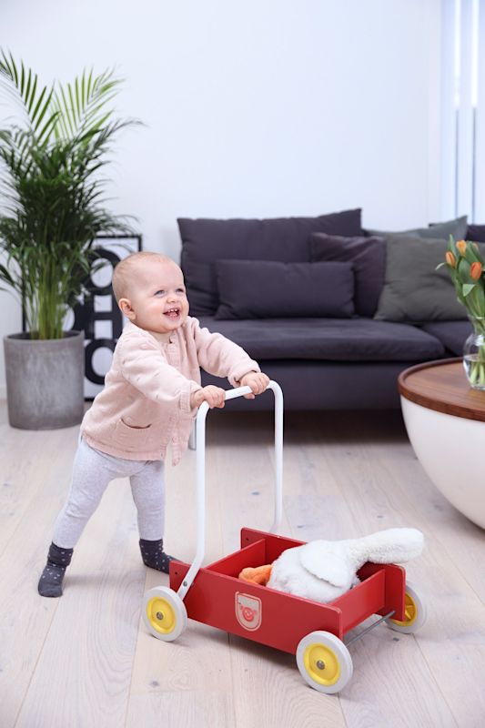 Lite barn i rosa genser dytter rød lekkevogn med kosekanin i lys, moderne stue
