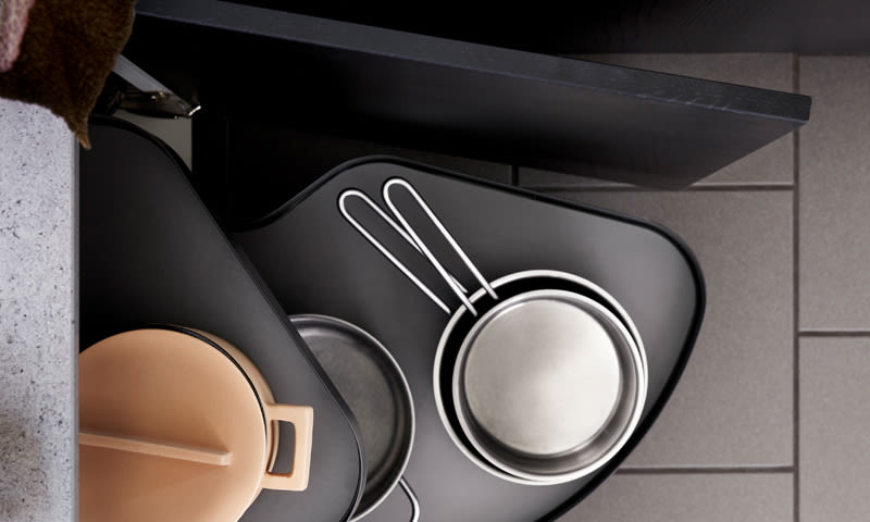 Åpnet kjøkkenskuff med svart uttrekkshylle, beige gryte med lokk og to stålpanner med hvite håndtak