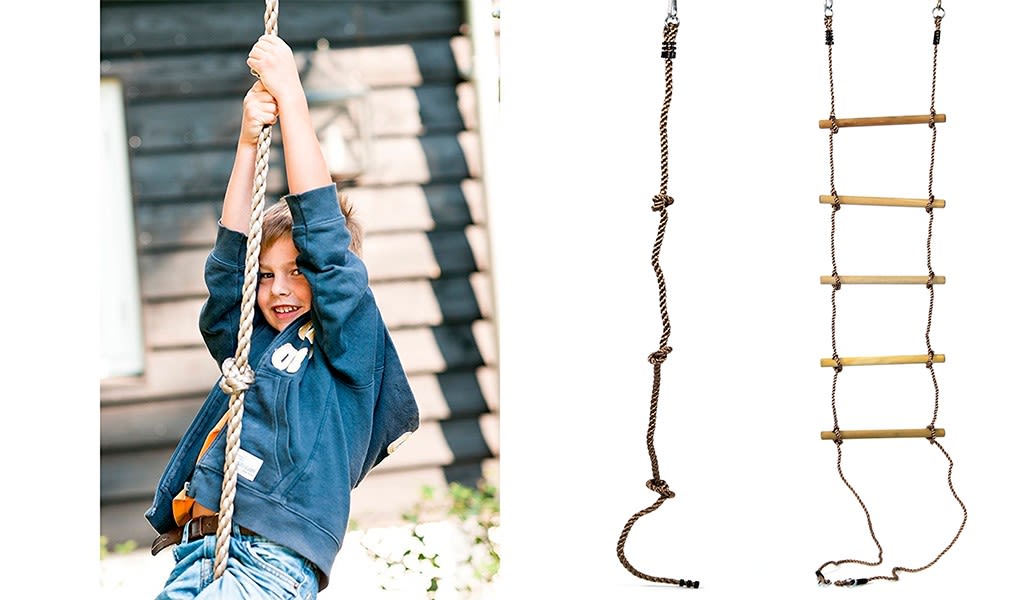 Barn i blå hettegenser klatrer beige tau foran trehus, to tau-stiger med knuter og tresperrer