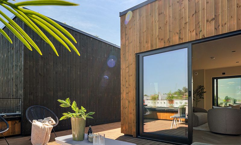 Moderne uteplass med sorte vinduer og lys brun kledning