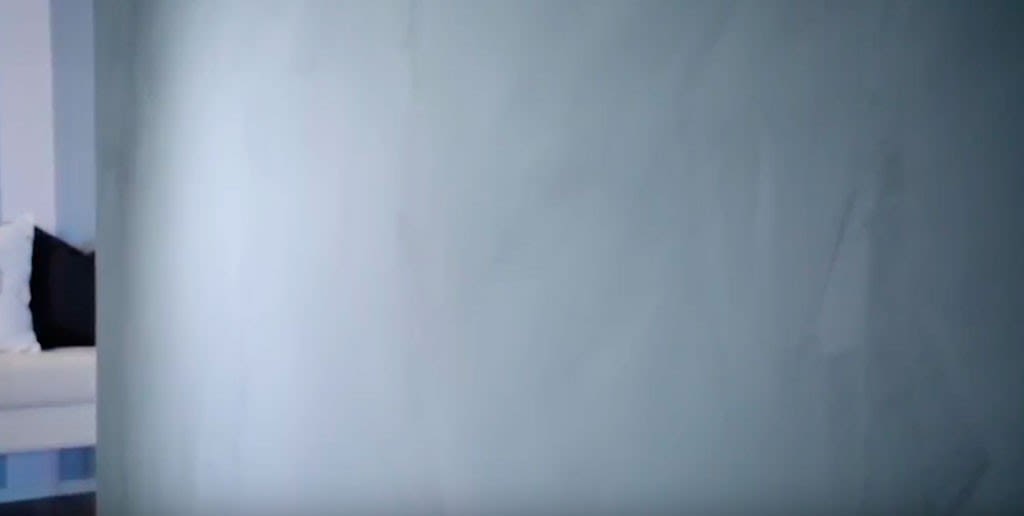 Ugjennomsiktig lyseblå glassvegg foran hvit sofa med svart pute i lyst oppholdsrom