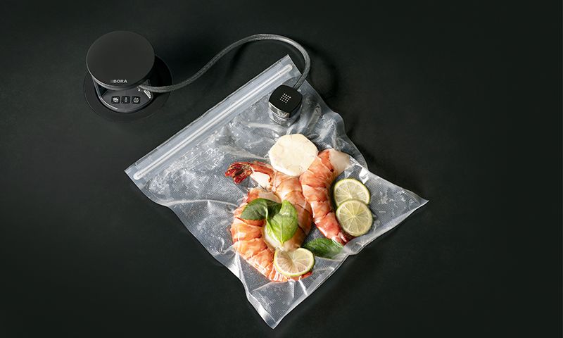 To rosa reker med lime, hvitløk og basilikum vakuumpakket i plastpose ved svart sous vide-maskin.