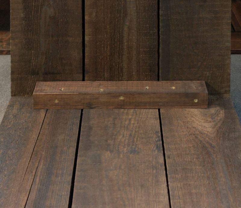 Mørkt trestykke med seks messingfargede skruer på mørk treakpanel over tregulv.