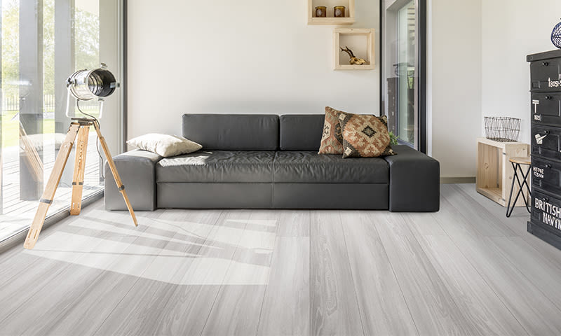 Lyst, minimalistisk stue med sort skinnsofa, mønstret pute, trebent gulvlampe og lyst tregulv