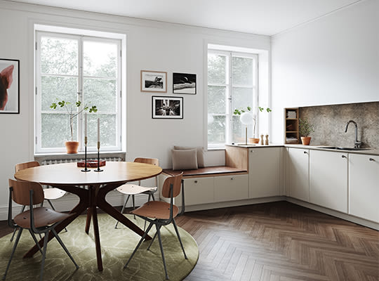 Lyst nordisk kjøkken med rundt trebord på grønt teppe, fire stoler og vindusbenk med planter.