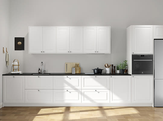 Hvit minimalistisk kjøkken med svarte benkeplater, tregulv, skjærebrett, gryte og grønne planter.