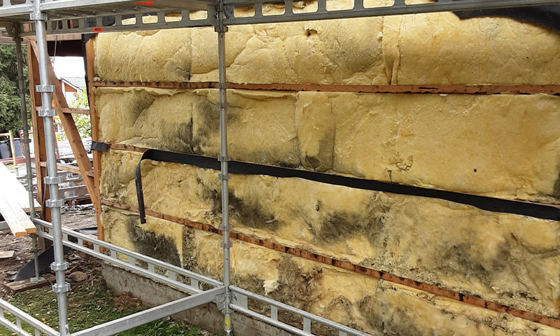 Stillas foran gul isolasjon med mørke flekker på vegg under rehabilitering.