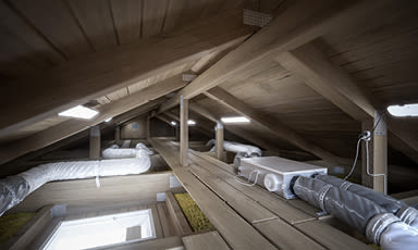 Loft med lyst treverk og LED-lys, synlige hvite/grå ventilasjonskanaler under skråtak