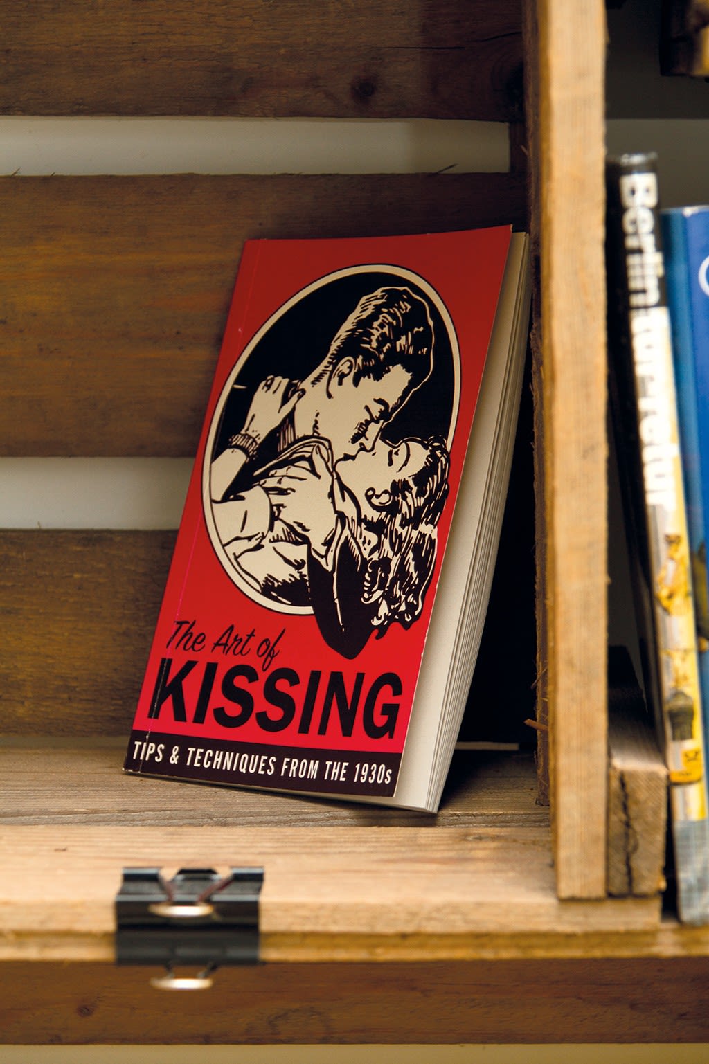 Rød bok med 1930-tallsillustrasjon av kyssende par stående på en trehylle.