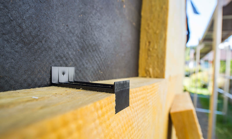 Nærbilde av gul trestender med svarte plastklips mot mørk underlagsduk på byggeplass