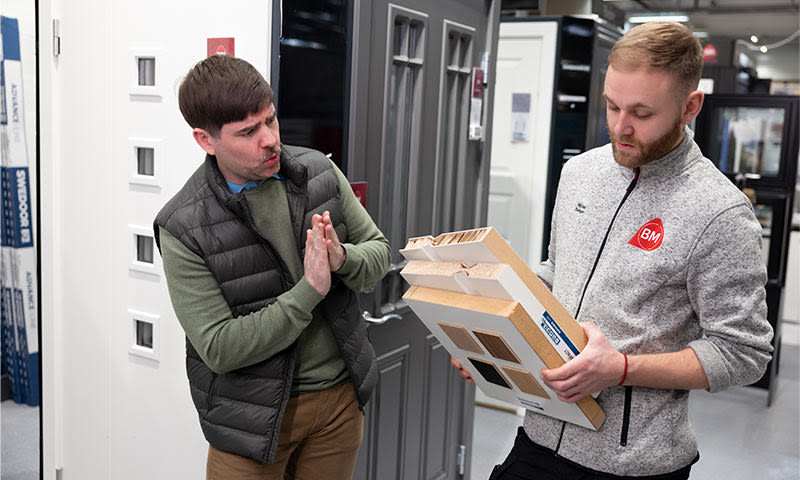 To menn ved dørutstilling, én viser snittmodell av flerlagsdør med vindu.