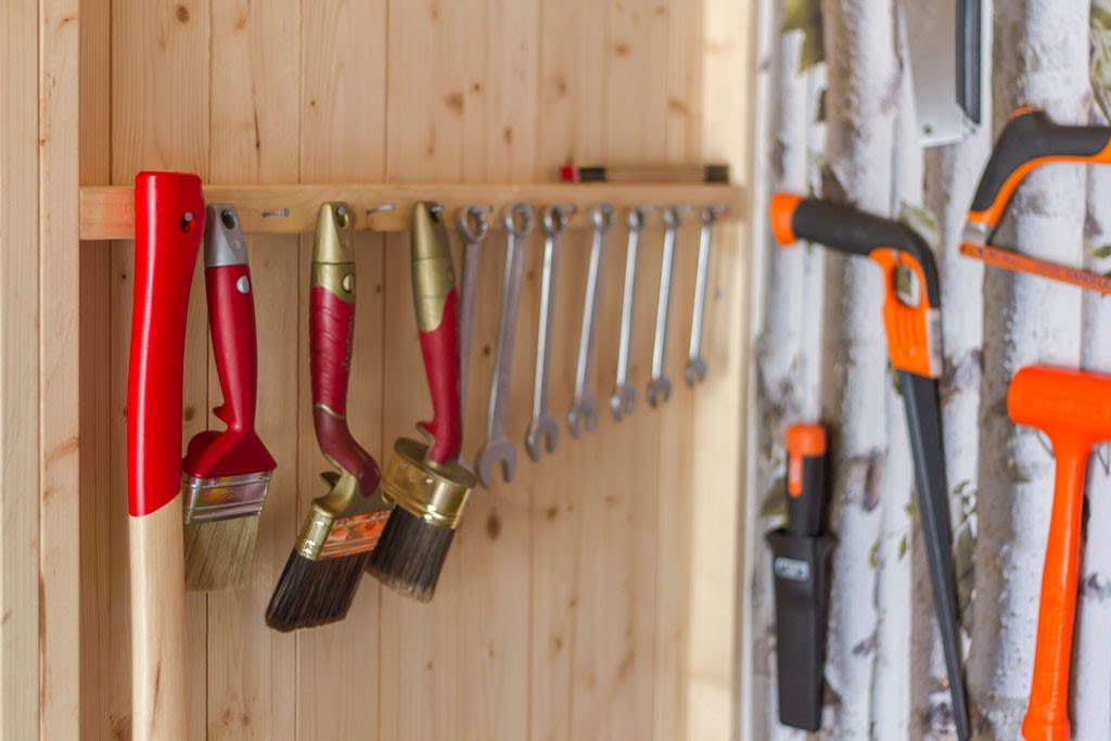 Røde malepensler, sølvfargede skiftenøkler og oransje verktøy på lys trevegg.