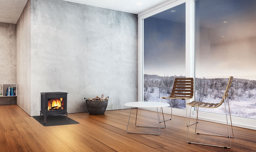 Lys stue med tregulv, peis i betonghjørne, kurv med ved, to tremøbler og snølandskap.