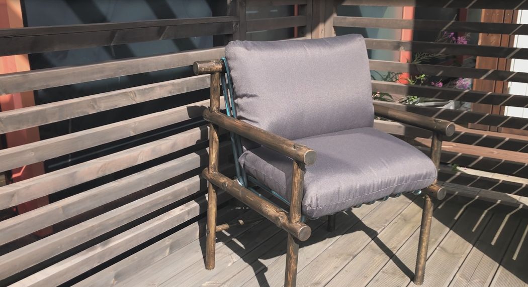 Rustikk stol i tre med grå pute på solfylt terrasse foran trepanel.