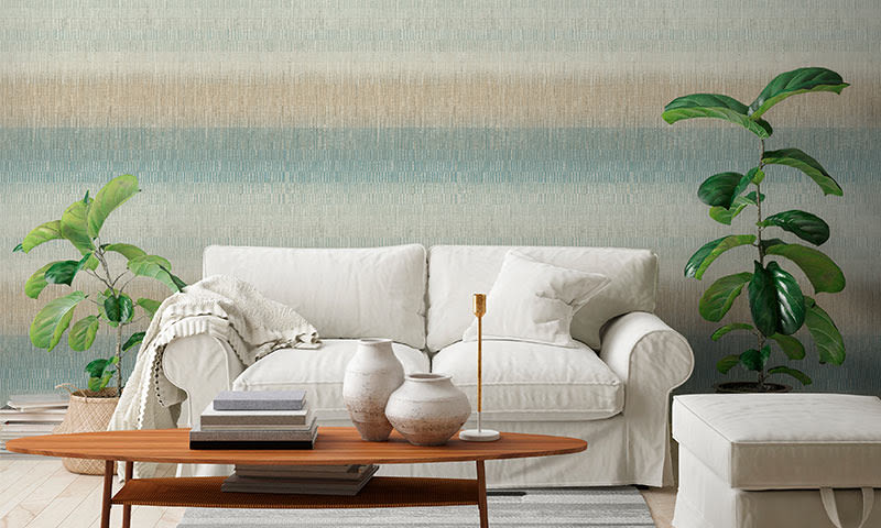 Hvit sofa med puter og pledd, trebord med vaser og bøker, grønne planter foran stripet vegg.