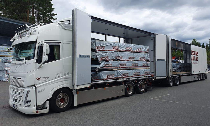 Hvit semitrailer med åpent sideplan og stabler plastinnpakkede trelastpakker fra Bergene Holm AS