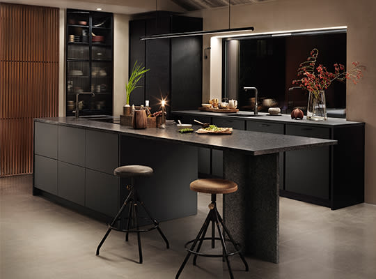 Moderne mørk grå kjøkkenøy med barstoler, glassvitrineskap, trepaneler og varm belysning
