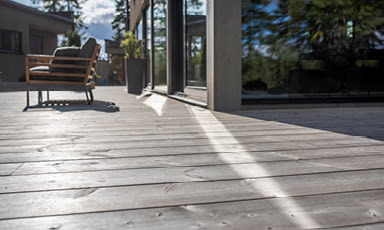 Lys treterrasse med moderne brun/beige stol, grønn potteplante og speilende glassdør.