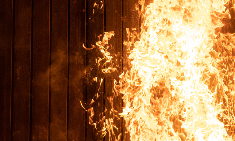 Kraftige oransje og gule flammer som sluker en mørk trevegg.