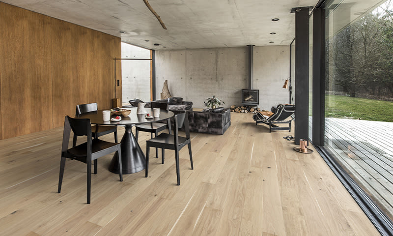 Moderne stue med lyst tregulv, betongvegg, svart spisebord, grå sofa, peis og store glassvinduer