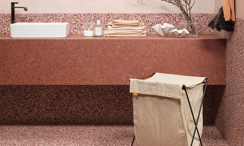 Moderne bad med rosa-terrazzo benk, hvit servant, sort kran, beige håndklær og lerretsvaskekurv