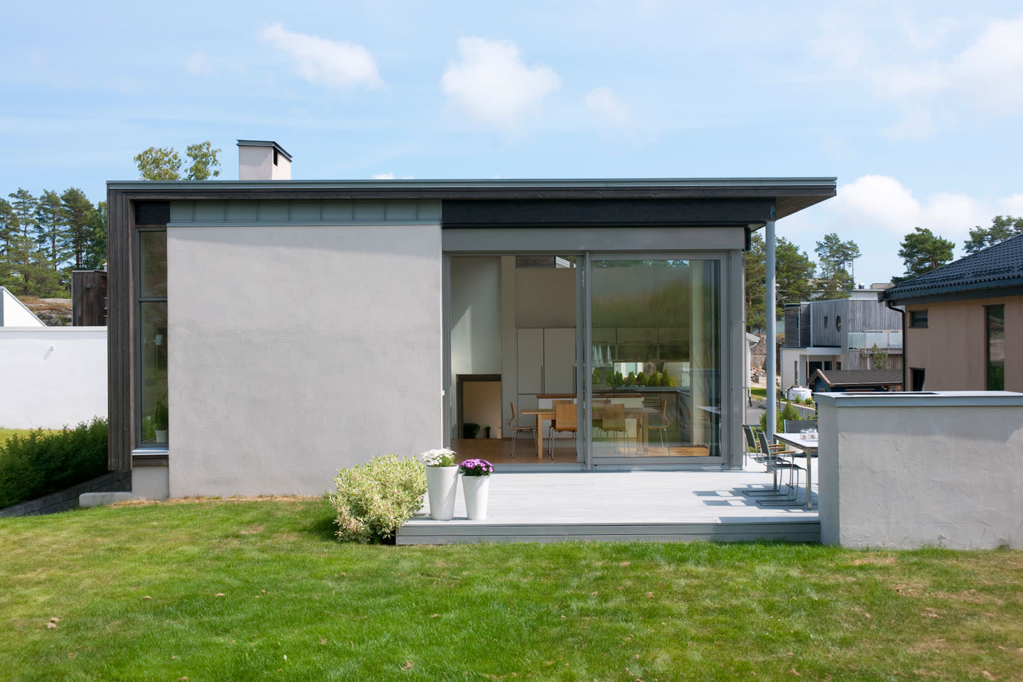 Moderne hvitgrå enetasjes bolig med store glassdører, grønt gress og hvite blomsterpotter.