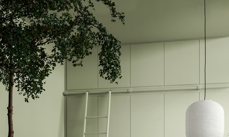 Minimalistisk rom med lysegrønne skap, hvit stige, hengende hvit papirlampe og trekvist.