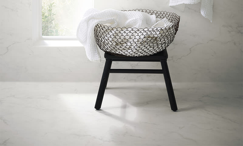 Svart metalltrådkurv med hvite håndklær på svart stativ ved solbelyst vindu i baderom.