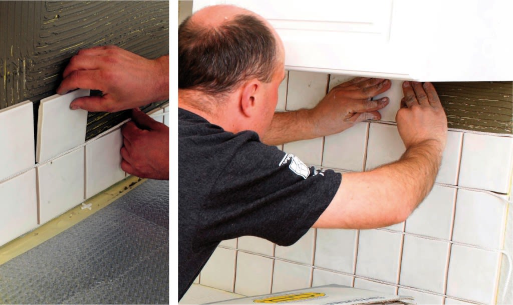 Hender monterer kvadratiske hvite fliser med grått lim på kjøkkenvegg under hvitt skap