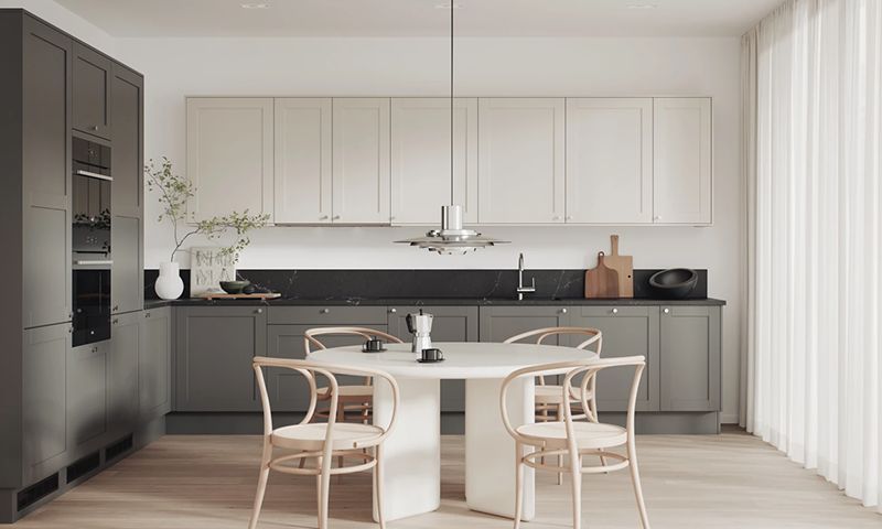 Moderne kjøkken med grå og hvite skap, svart benkeplate, rundt hvitt bord og beige stoler.