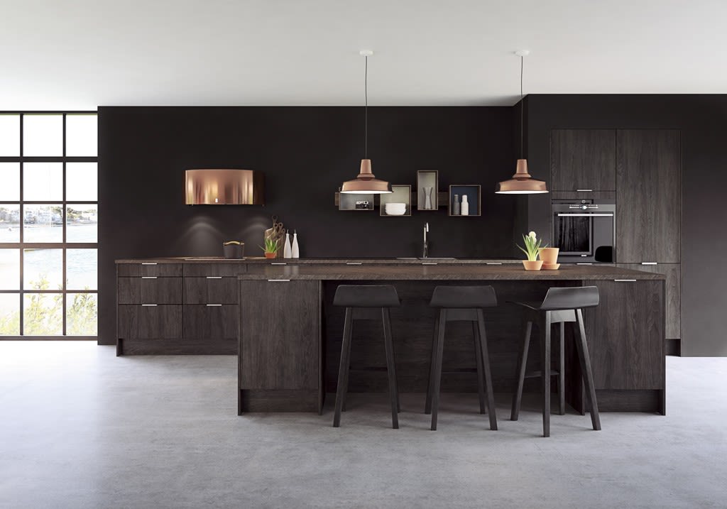 Moderne kjøkken med mørke treflater, svart øy med krakker, kobberpendler og sjøutsikt.