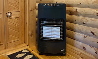 Svart bærbar gassovn med hvite keramiske plater i hjørne av lys tømmerhytte.