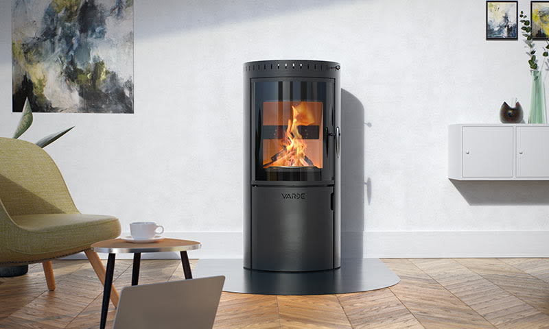 Minimalistisk stue med svart sylinder-vedovn i flammer, grønn lenestol, trebord med hvit kopp