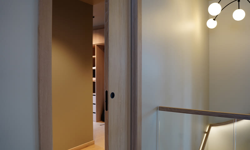 Åpen skyvedør i lyst tre mot gang med glassrekkverk og varm belysning.