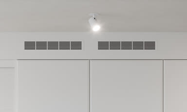 Hvit minimalistisk vegg med tre paneler, innebygde ventiler og ett takspot.