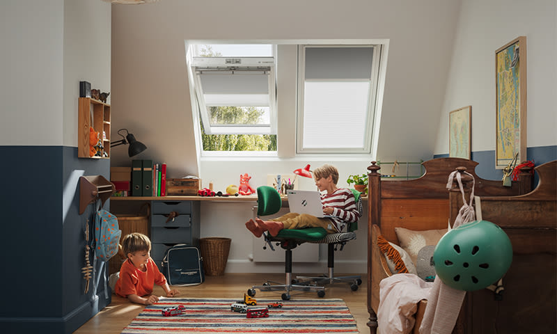 Barnerom med skråtak, blå vegger, skrivebord med laptop og kontorstol, gulvlek med biler