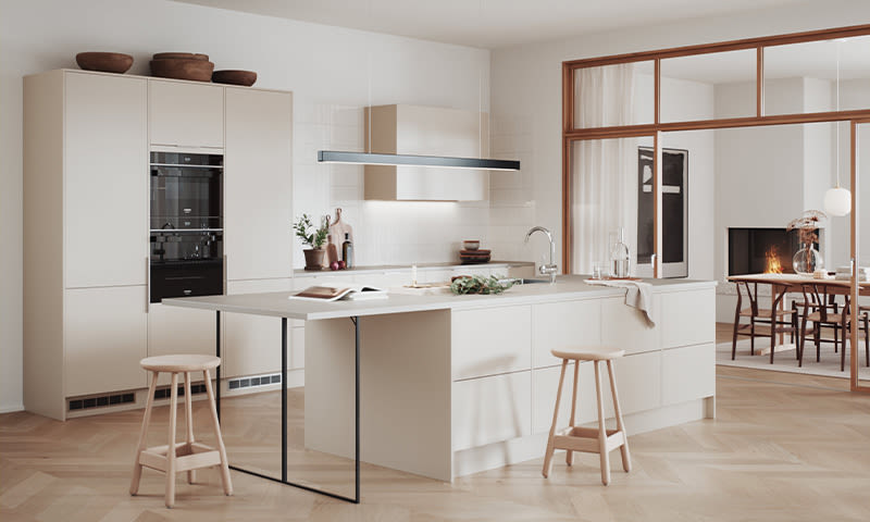 Moderne lysebeige kjøkken med øy, to barkrakker og åpen spisestue med peis.