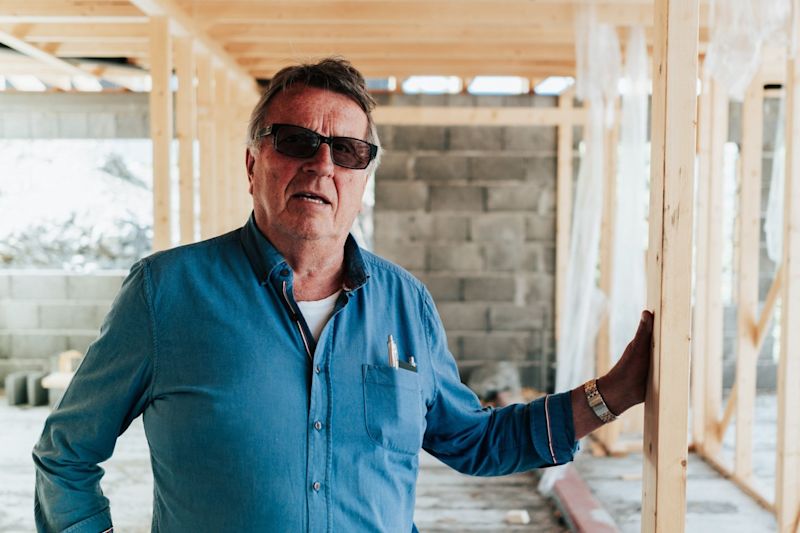 Mann i blå skjorte holder trestender i hus under oppføring med synlig betongvegg