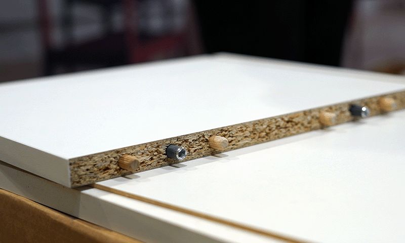 Hvit laminatplate med sponplatekjerne, treplugger og metallinnsatser langs kanten.