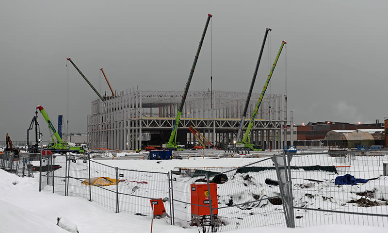 Snødekt byggeplass med stålramme og grønne kraner under grå, tåkelagt himmel